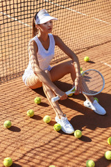 Young attractive brunette girl in stylish tennis outfit poses on the court with a racket and tennis balls.