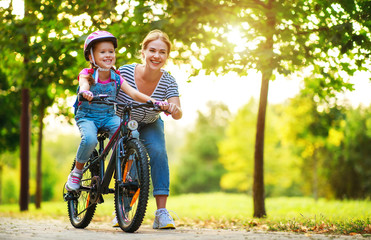 happy family mother teaches child daughter to ride a bike in the Park