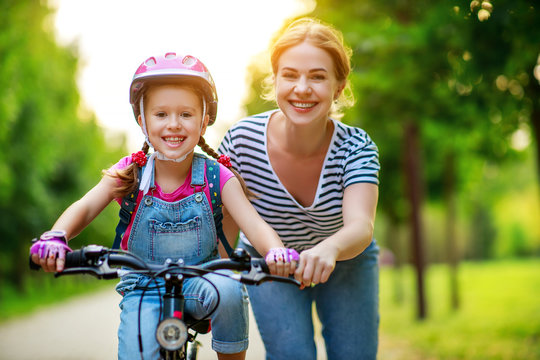 happy family mother teaches child daughter to ride a bike in the Park - Powered by Adobe