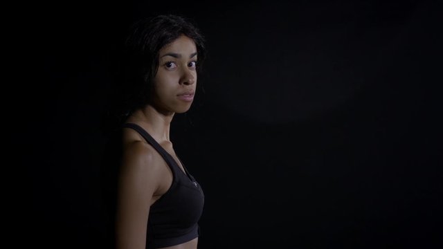 MS mixed race woman walks into frame in soft focus profile with black background. She stops and comes into focus as she looks to camera HD