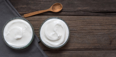 White yogurt in two glass bowls on old wooden desk with old wooden spoon.