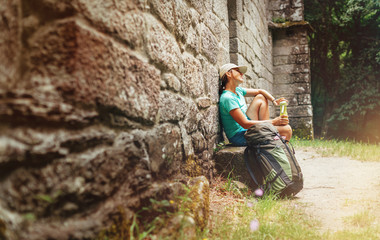 Obraz na płótnie Canvas Tired female backpacker resting on the bench near the old antique brick wall castle on the famous Camino de Santiago way.