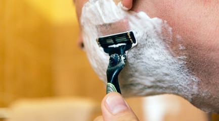 Man shaving his face with the razor blade through shave foam. Men skin care concept.