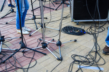 Close up view of tangled black wires and cables plugged and microphone stand on the ground, chaos after concert