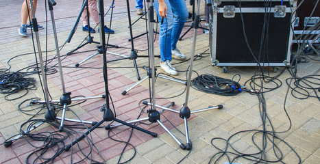 Close up view of tangled black wires and cables plugged and microphone stand on the ground, chaos after concert