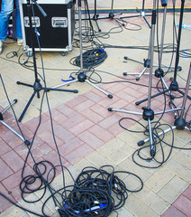 Fototapeta na wymiar Close up view of tangled black wires and cables plugged and microphone stand on the ground, chaos after concert