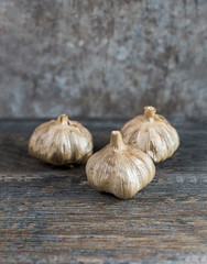whole black garlic in half on a rustic wooden table  with textured background, moody product photo, food image with negative space for title
