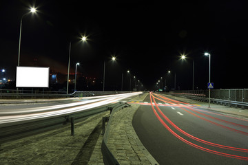 Smugi świateł samochodów w nocy na autostradzie, bilbord reklamowy.