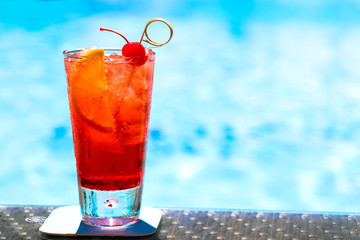 glass of bright red tropical cocktail on a background of blue pool water