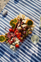 Summer picnic on the sea beach at sunset. tray of tasty appetizers and glasses with sparkling wine on a striped beach towel. Cucumis metuliferus or Kiwano in the center of the composition.