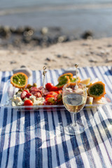 Summer picnic on the sea beach at sunset. tray of tasty appetizers and glasses with sparkling wine on a striped beach towel. Cucumis metuliferus or Kiwano in the center of the composition.