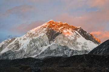 As the sun sets in Nepal, an orange glow lights up the snowcapped rocky Himalayan mountains