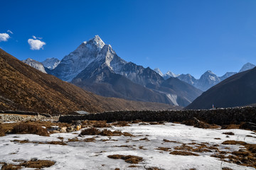 A farm field covered in ice with a stone fence plotting the available land and the Himalayan mountains in the background on a clear and sunny day
