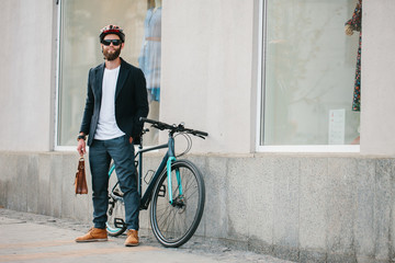 A young stylish hipster businessman going to work by bike on urban street.