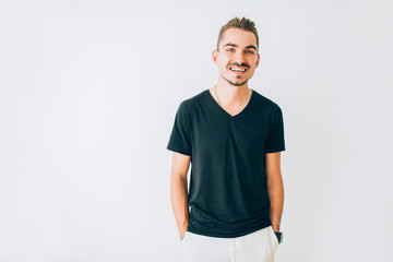 Fototapeta premium Happy young guy in black t-shirt posing on white isolated background with hands in pockets.