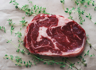 Raw fresh ribeye steak with fresh thyme on white paper top view