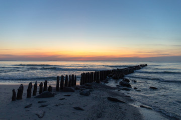 Fototapeta na wymiar beautiful natural scene, old breakwaters in the sea at dusk against the background of an orange sunset