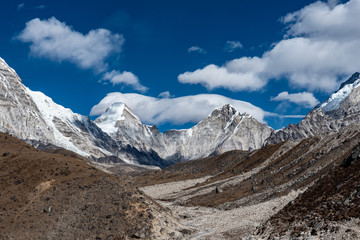 A view of the brown rocky valley surrounded by snowcapped grey mountains on a partially cloudy day in the Nepalese Himalayas - Powered by Adobe