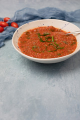 Homemade Chunky Tomato Soup on Textured Blue Background with Tomatoes and Basil in Background