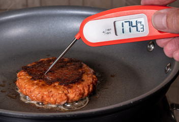 Charred and ready to eat plant-based burger in frying pan with instant thermometer confirming...