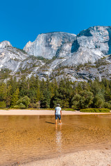 Mirror lake, a young man in a white shirt walking along the lake water and the sun in the background. California, United States