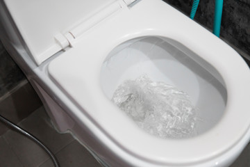 Water flushing in toilet bowl. White hanging toilet seat on white toilet in the home bathroom with...