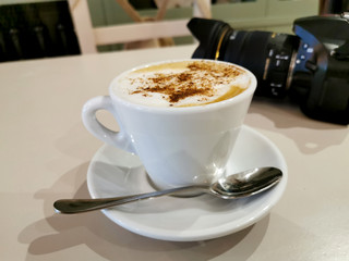Taza de capuchino caliente junto a cámara