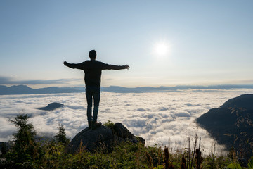 hiker celebrating success on top of a mountain above the clouds. Young man enjoying freedome, Mountaineering sport lifestyle concept