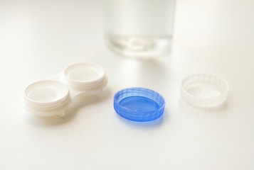 Accessories for the proper use of contact lenses: case, tweezers and bottle of solution on white background. Safe vision correction. Selective focus.