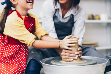 Happy mother and daughter making clay pottery on a spin wheel. .