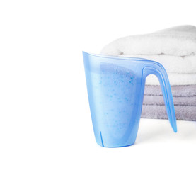 Laundry detergent in plastic measuring cup and towels on white background
