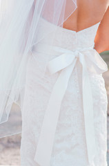 woman facing away wearing white lace wedding dress with buttons down the back, white ribbon sash tied in a bow, and a white veil