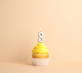 Birthday cupcake with number eight candle on beige background