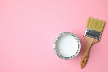 Open can with white paint and brush on pink background, flat lay. Space for text