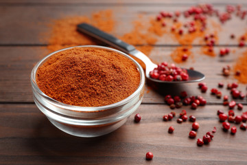 Bowl of red powdered pepper and spoon with corns on wooden table, space for text