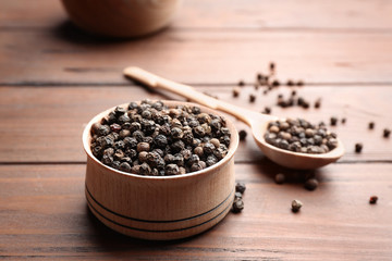 Bowl of black pepper corns and spoon on wooden table, space for text