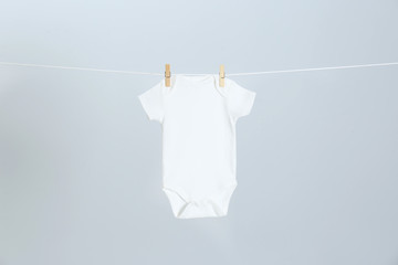 Cute baby onesie hanging on clothes line against light grey background. Laundry day