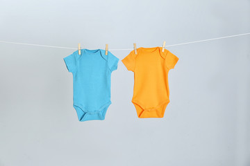 Different baby onesies hanging on clothes line against light grey background. Laundry day