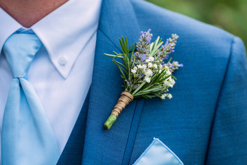 boutonniere made with lavender, rosemary, and babys breath tied with twine pinned to a blue jacket,...