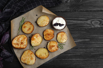 Delicious potato wedges with sour cream on black wooden table, flat lay