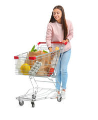 Young woman with full shopping cart on white background