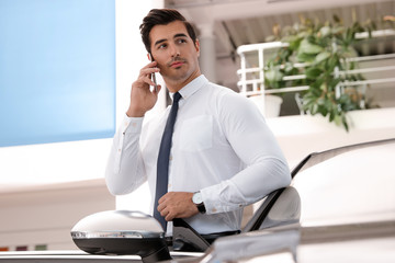 Young man talking on phone near car in modern dealership