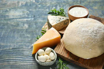 Fresh dough and pizza ingredients on blue wooden table. Space for text