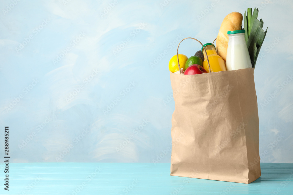 Wall mural paper bag with groceries on wooden table against light blue background. space for text