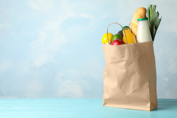 Paper bag with groceries on wooden table against light blue background. Space for text