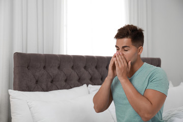 Young man suffering from allergy in bedroom