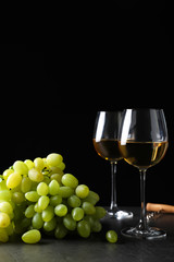 Fresh ripe juicy grapes with wineglasses on grey table against black background, space for text