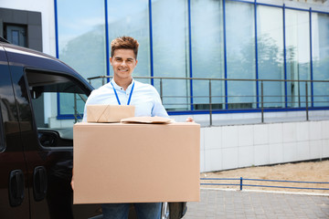 Young courier holding parcels near delivery car outdoors. Space for text