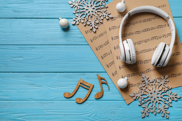 Flat lay composition with Christmas decorations, headphones and music sheets on blue wooden table, space for text