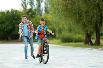Obraz na płótnie Canvas Dad teaching son to ride bicycle in park